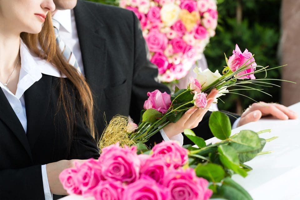people holding pink flowers over a funeral coffin